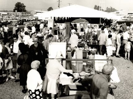 Past era shoppers at outdoor market event.